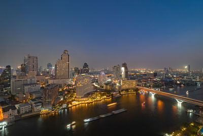 Illuminated buildings by river against sky in city at night