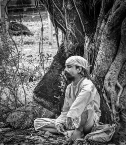 Side view of young woman sitting on tree trunk