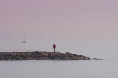 Man standing on rocks in sea against sky