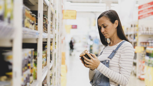 Side view of woman looking at bottle in supermarket