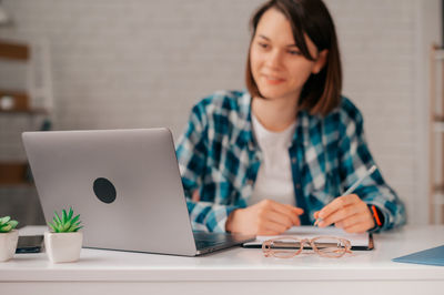 Young woman using mobile phone while sitting on table