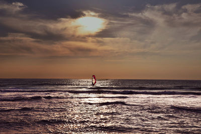 Man standing in sea against sky during sunset