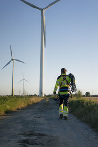 Technician walking on field path at a wind farm with climbing equipment