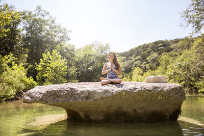 Side view of woman sitting on rock by lake