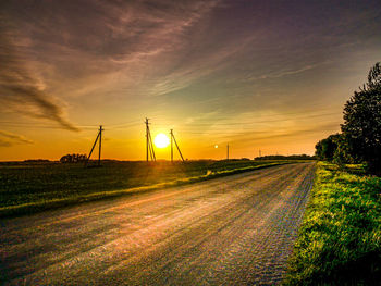 Road amidst field against sky during sunset