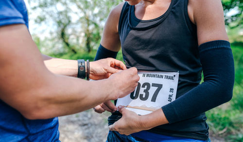 Midsection of woman attaching marathon bib while standing in forest