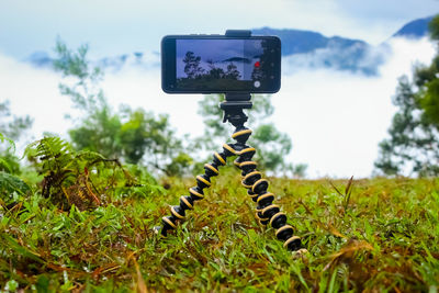 Close-up of digital camera on field against sky