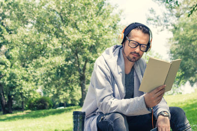 Mature man listening music while reading book in park