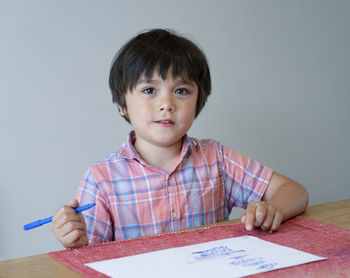 School kid boy siting on table doing homework, child  boy drawing blue colour on white paper 