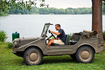 Young man sitting on off-road vehicle on grassy field by lake