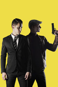 Businessman and gangster looking away while standing against yellow background