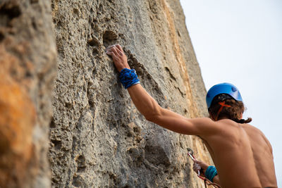 Close-up of shirtless man rock climbing against sky