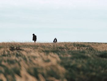 Rear view of people standing on field against sky