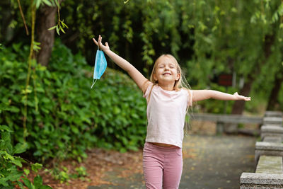 Cheerful girl holding mask running against trees