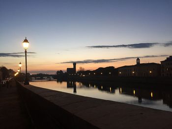 Illuminated city by river against sky at sunset