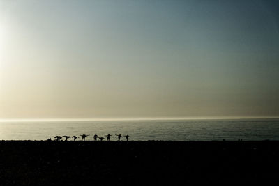 Silhouette people on beach against clear sky