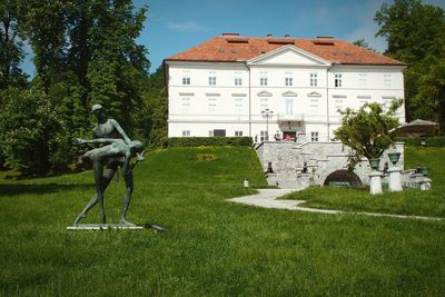 Statue on grassy field by house and trees