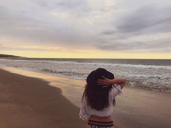 Rear view of woman standing on beach against sky