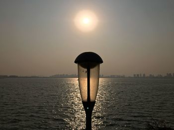 Lamp post in sea against clear sky during sunset