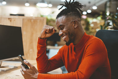 Excited businessman looking at smart phone cheering in office