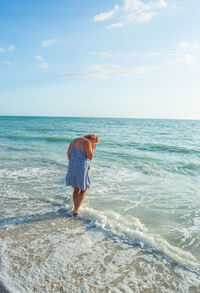 Woman wading in sea against sky