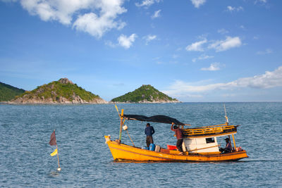 Men on boat in sea against blue sky