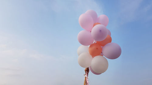 Flying balloons of delicate pink and white coral colors in female hand on background of blue sky 