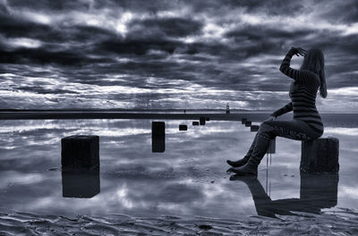 Side view of woman sitting by sea against sky