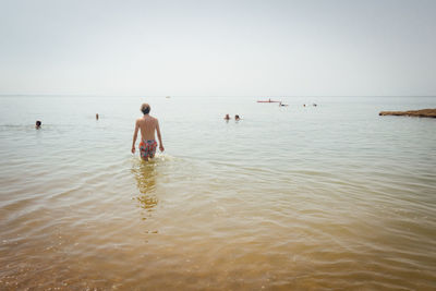 Rear view of man standing in sea against clear sky