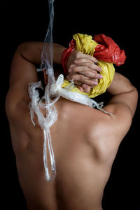Rear view of shirtless young man with plastic against black background