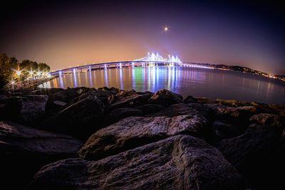 Illuminated bridge over river against sky at night