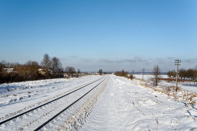 Snow covered railroad tracks against clear sky during winter