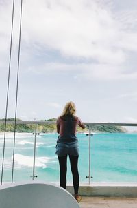 Rear view of woman standing by sea against sky