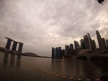 Sea by modern buildings against sky during sunset