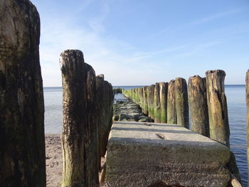 Narrow wooden posts in calm sea against blue sky