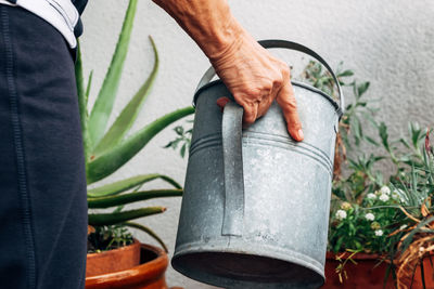 Unrecognizable aged woman watering decorative plants and flowers during gardening on balcony