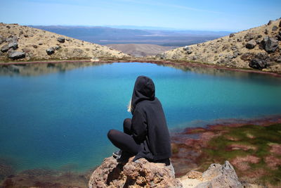 Rear view of man sitting on rock by lake