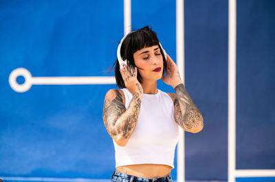 Caucasian girl with tattoos on her body listening to music with headphones on the street