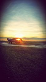 Airplane on runway against sky during sunset