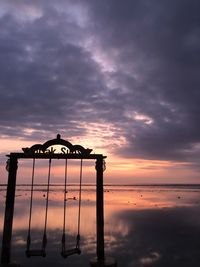 Silhouette lifeguard hut on beach against sky during sunset