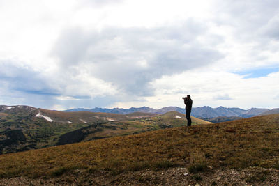 Full length of man photographing on mountain against cloudy sky