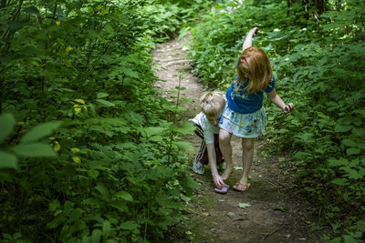Brother assisting sister in wearing flip-flop at forest