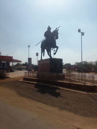 Statue by railroad tracks against sky in city