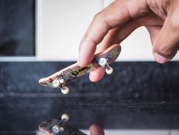 Cropped hand holding toy skateboard over floor
