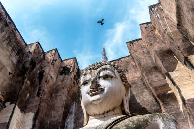 Low angle view of statue by historical building against sky