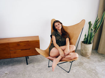 Young woman sitting on chair against wall