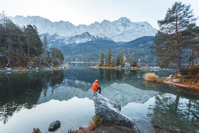 Rear view of man sitting by lake on rock