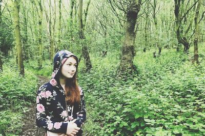 Girl looking away while standing by plants in forest