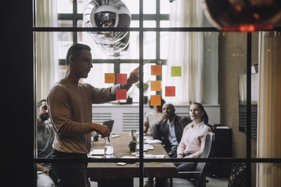 Mature businessman discussing over adhesive notes with colleagues in meeting room