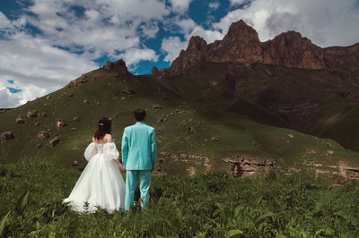 Bride and groom holding hands near a mountain against a cloudy sky in a natural park. a wedding